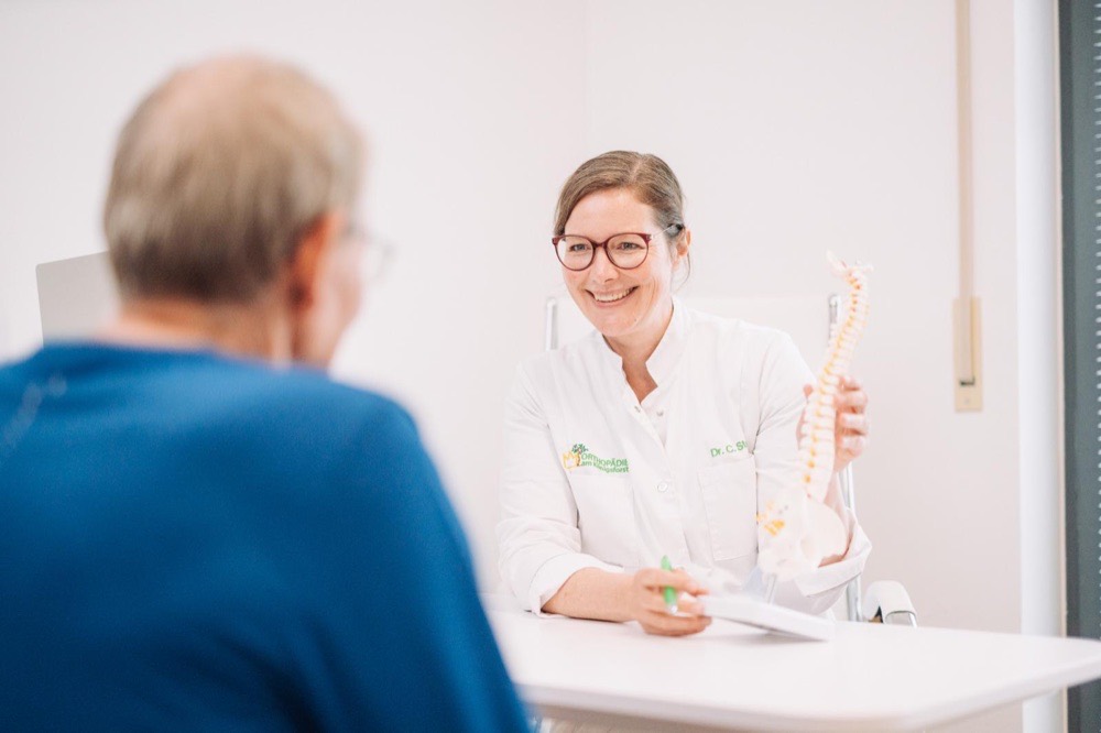Dr. med. Claudia Stock erklärt im Patientengespräch die Wirbelsäulen-Schmerztherapie anhand eines Wirbelsäulenmodells